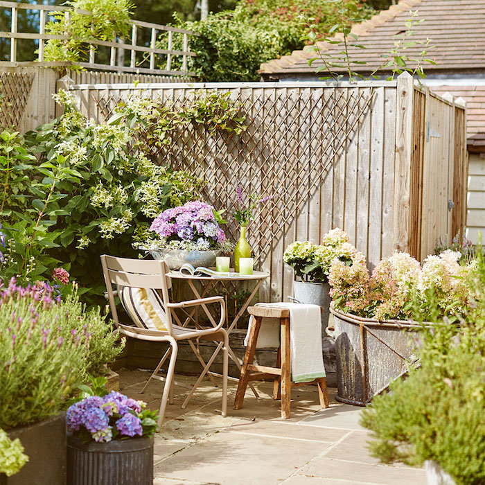 decoration jardin terrasse en dalles de pierre, table, tabouret et chaise metallique simples, mur de bois, plantes en bacs