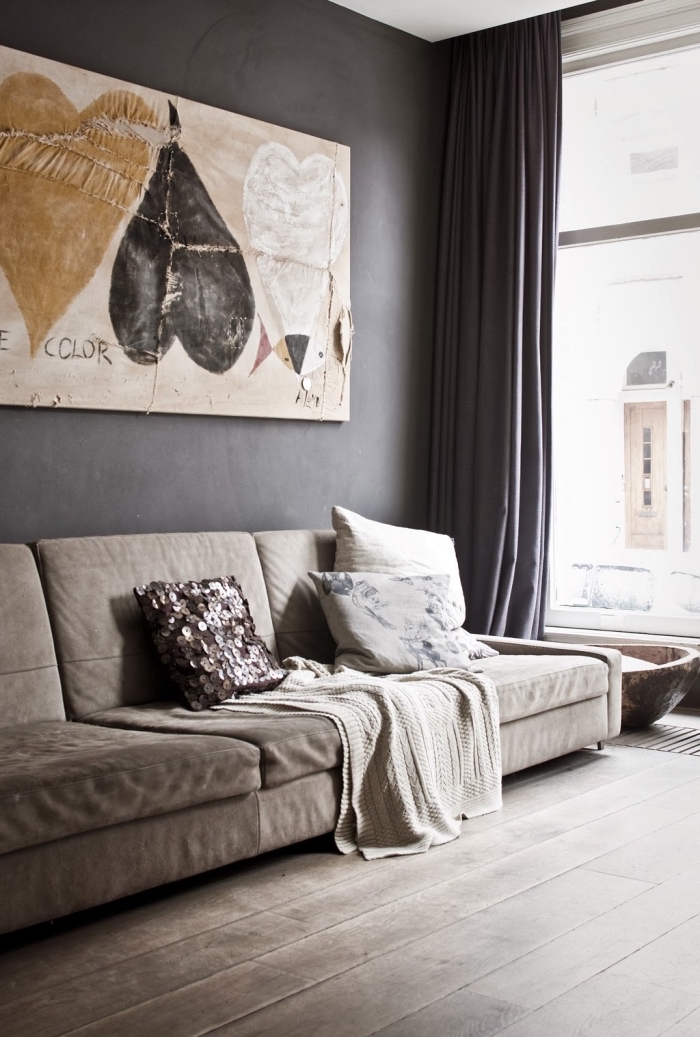 aménagement de salon avec grande fenêtre et murs foncés, modèle de canapé long de couleur beige sur un parquet de bois foncé