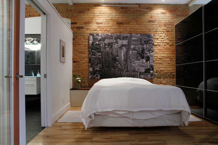 exemple de décor industriel avec mur de briques, panneau décoratif noir et blanc, style new york, linge de lit blanc, armoire noire