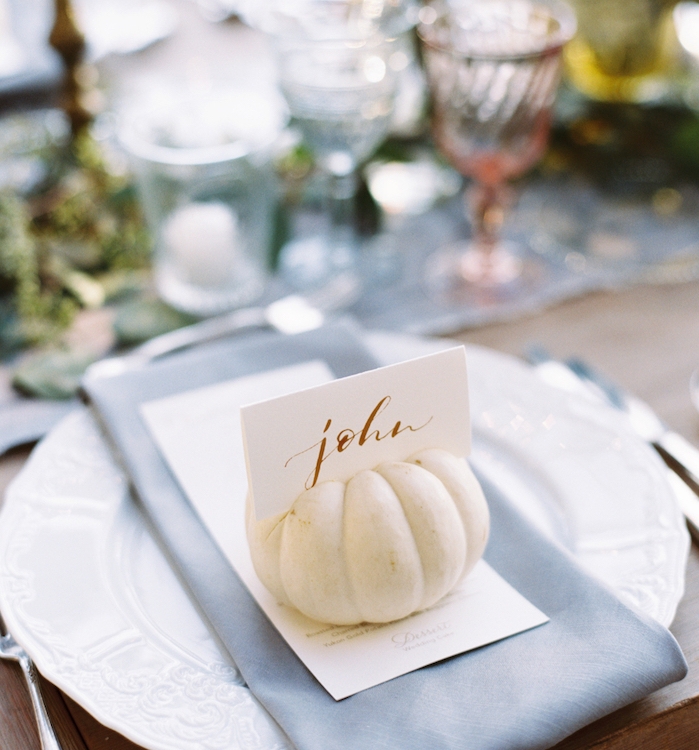 petite citrouille avec étiquette blanche nom écrit en lettres or calligraphie, assiette blanche, serviette gris, centre de table floral