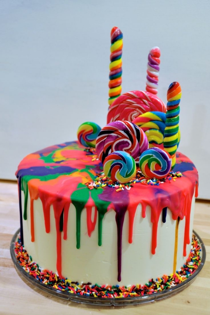 idée pour un gateau cake design original au glaçage coulant arc-en-ciel décoré avec des sucettes colorées