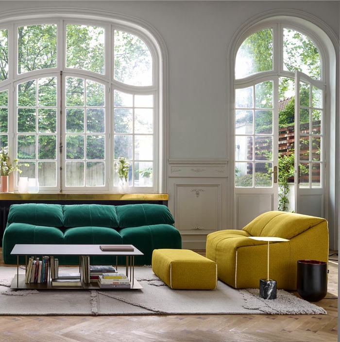 grandes fenêtres arcs dans un salon spacieux à l'équipement minimaliste, sofa vert et canapé jaune avec tabouret