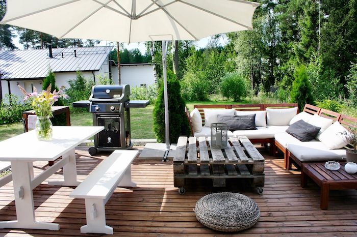 decoration jardin terrasse en bois avec une table basse en palette à roulettes, canapé bois, coin repas en bancs et table blanches, barbecue