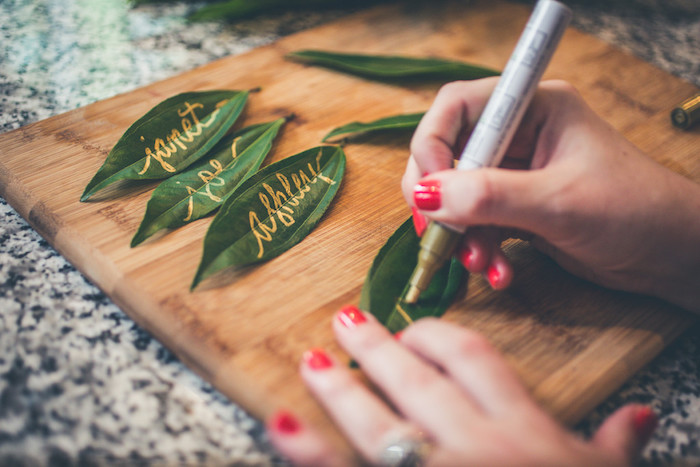marque place mariage en feuilles vertes avec écriture feutre or nom de l invité, décoration de table florale originale