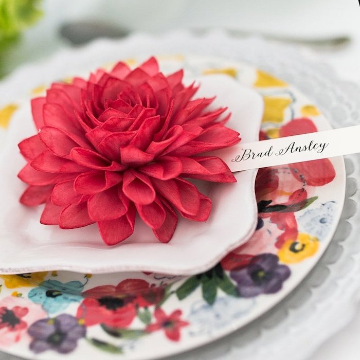 porte nom mariage en fleur de tissu rouge dans assiettes, assiette blanche et assiette fleurie, nom invité sur bout de papier