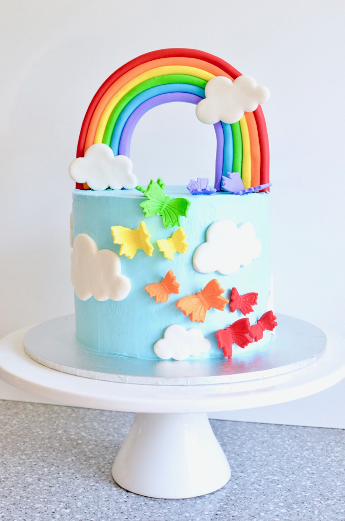 comment faire un gateau d'anniversaire arc-en-ciel au glaçage bleu ciel décoré, décoration de gâteau originale de nuages et papillons modelés en pâte à sucre