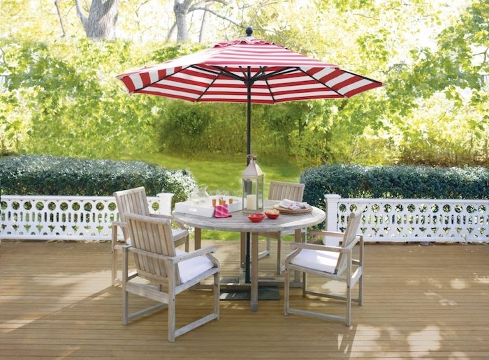 décoration terrasse en bois avec table et chaises bois brut et parasol rouge et blanc, gazon vert bordé de buis verts