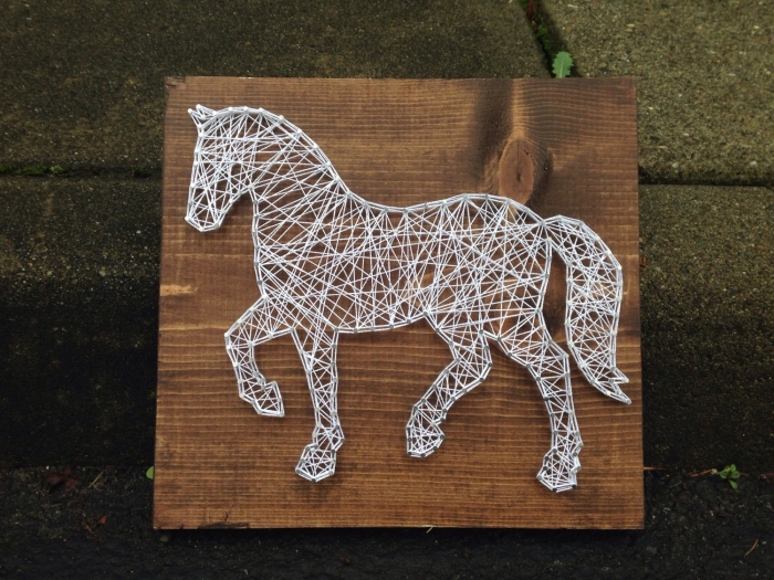 jolie déco murale DIY fait avec une planche de bois foncé et un fil blanc enrouler autour de clous en forme de cheval
