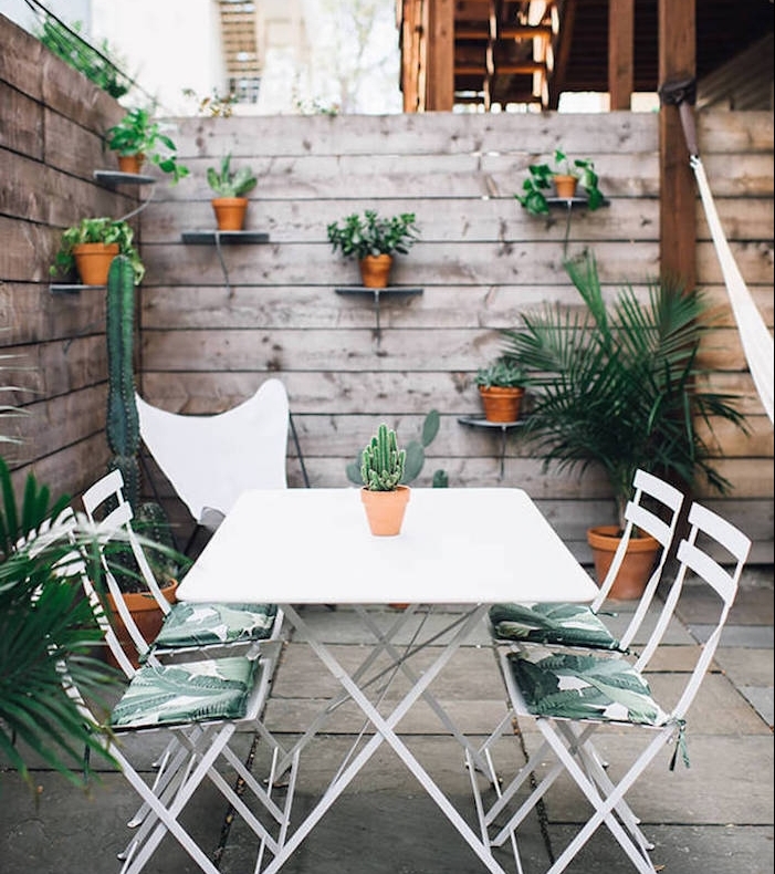 amenagement terrasse exterieure beton avec coin repas en table et chaises métalliques, clôture bois avec rangements pots de fleurs intégrées