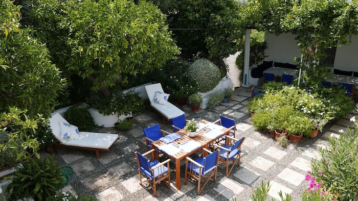dalles de béton et gravier sur une terrasse exterieure moderne, chaises longues, table et chaises en bois, plantes en pots et arbres en mordure
