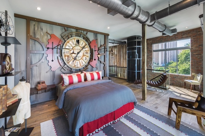 tuyaux apparentes dans une chambre style industriel, linge de lit rouge et gris, mur de briques, horlogerie murale sur mur d accent, parquet bois