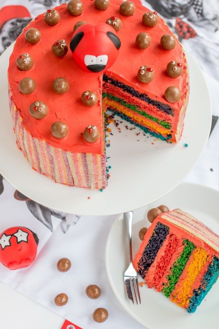 recette de gâteau arc en ciel original recouvert de glaçage rouge et décoré avec des bonbons au chocolat et des rubans acidulés 