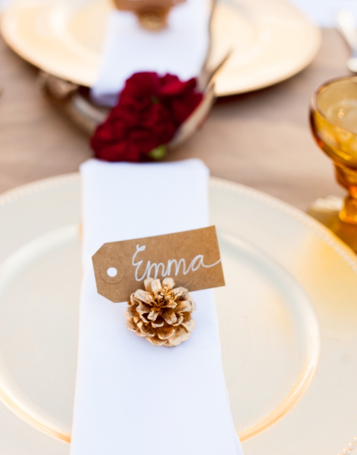 etiquette mariage papier kraft inséré dans une pomme de pin, serviette en tissu blanc, nappe marron et fleur rouge au centre