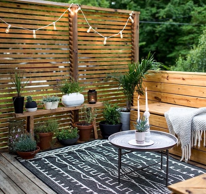 exemple d amenagement terrasse exterieure en banc de bois, tapis noir et blanc, revetement bois, panneau occulant bois, jardiniere palette, guirlande lumineuse, plantes vertes
