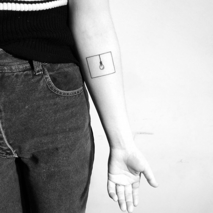 superbe exemple de petit tatouage femme sur la main à design abstrait avec une ampoule électrique encadrée