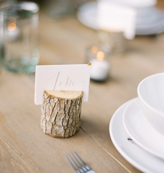 petit buche de bois avec fente pour insérer une etiquette mariage blanche, sur une table bois brut, vaisselle blanche