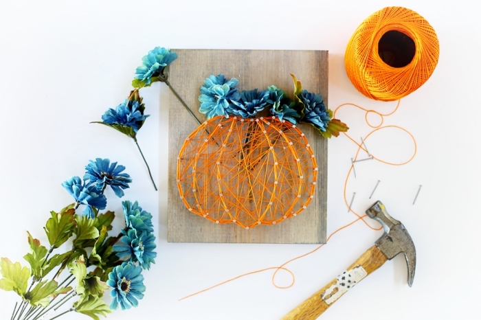 idée bricolage de Halloween avec planche de bois joliment décorée en fil tendu orange et fleurs artificielles bleues en forme de citrouille 