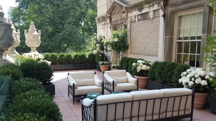 exemple aménagement de jardin terrasse en carrelage, canapé et chaises metalliques avec coussins blancs, buis taillés, art vintage, maison vintage
