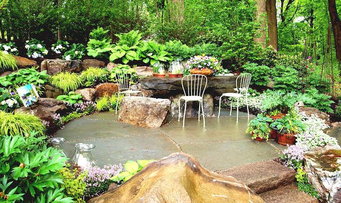 aménagement de jardin terrasse extérieure en pierre, rocaille fleurie, table en pierre naturelle et chaises metalliques, coin repas exterieur
