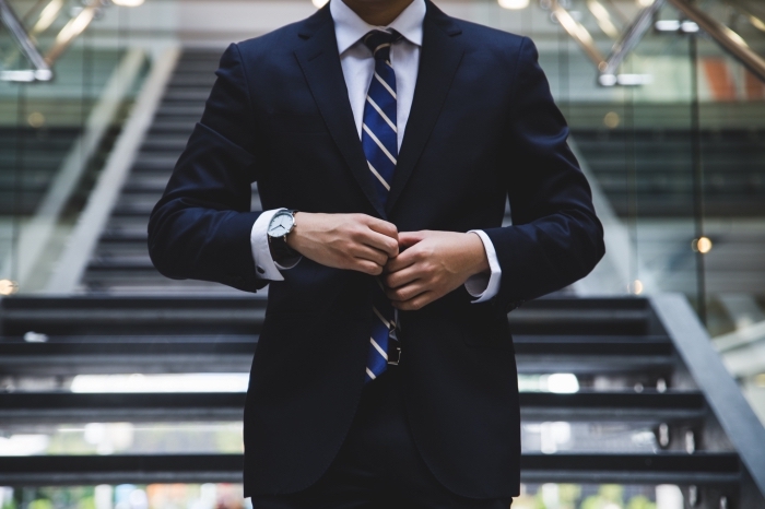 look homme élégant avec tailleur raffinée en bleu marine et chemise blanche accessoirisés avec cravate bleu marine rayée