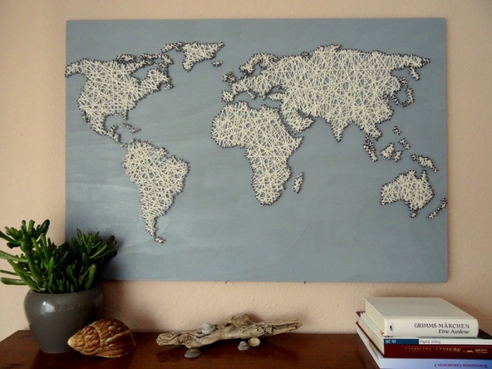 grand tableau de bois peint en bleu clair avec carte du monde en fil blanc et contours à fil noir comme un objet diy facile