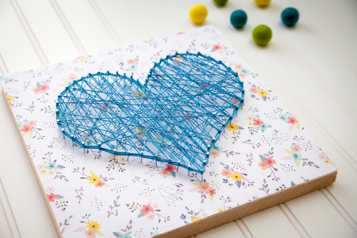 jolie création DIY sur une planche de bois de forme rectangulaire couverte de papier scrapbooking coloré et de fil bleu