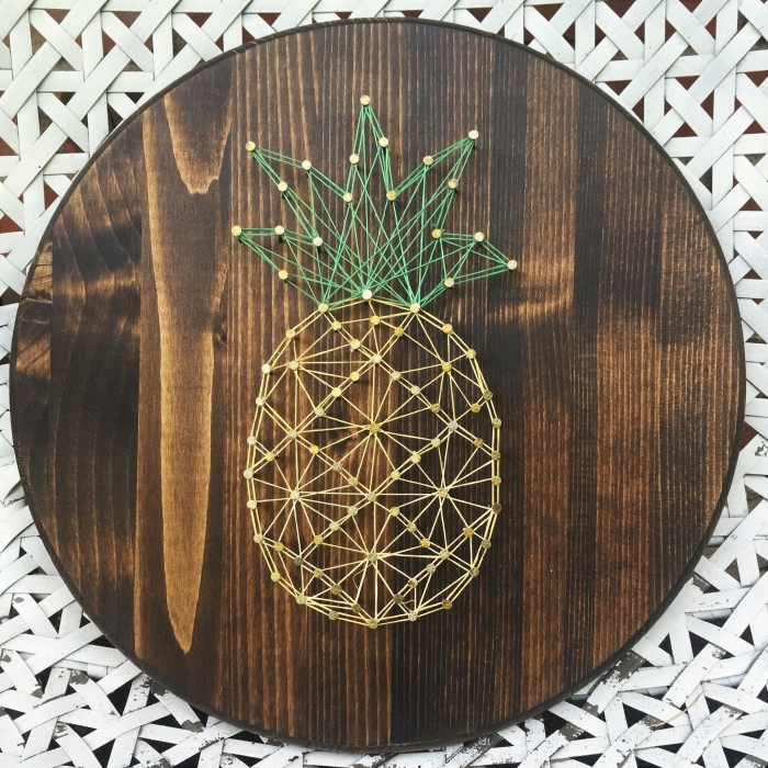 joli objet décoratif fait main avec un gabarit fil tendu à design ananas jaune et vert sur une planche de bois ronde