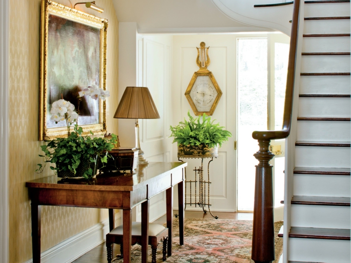 table en bois pour le hall d'entrée, lampe à abat-jour, peinture au cadre doré, tapis vintage, plantes vertes