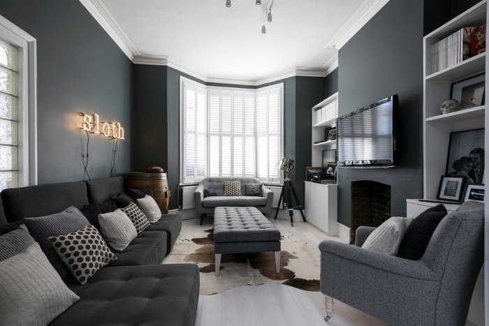 ambiance cozy dans un salon au plafond blanc et murs foncés avec meubles moderne, modèle de canapé gris foncé couvert de coussins