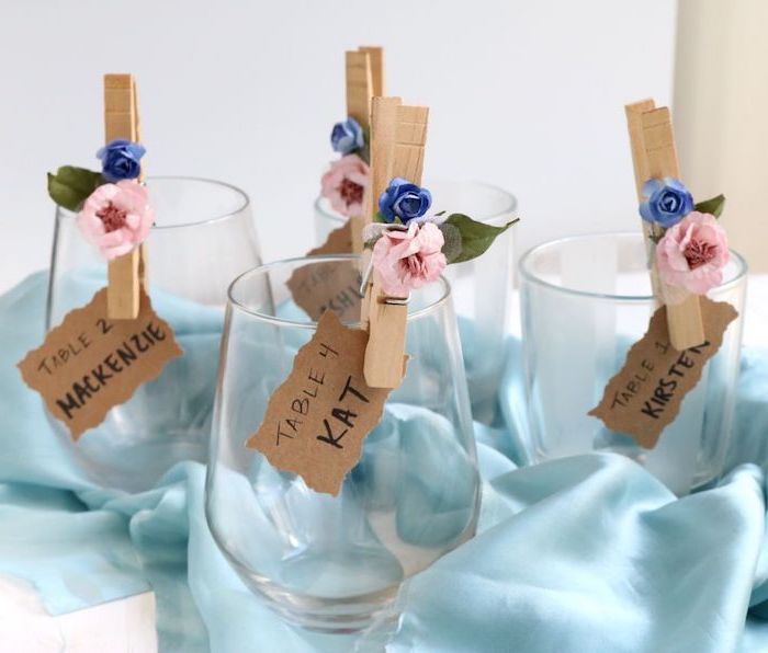 porte nom en pince à linge bois décoré de petites fleurs artificielles, toile de soie bleue, nappe blanche