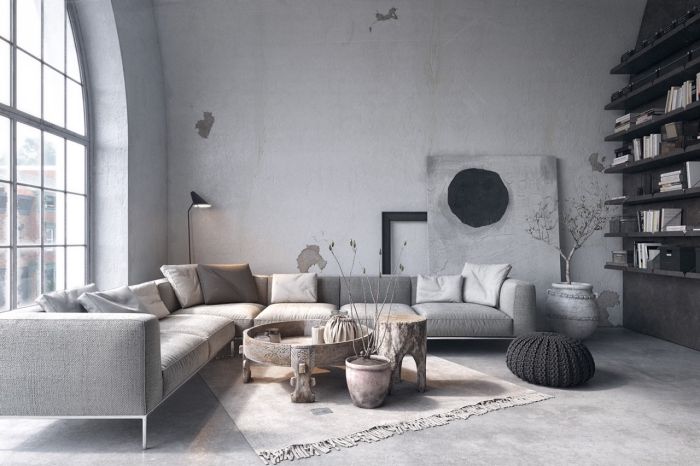 déco de style loft dans un salon aux murs gris clair et plancher imitation béton aménagé avec canapé d'angle couvert de coussins de couleurs neutres