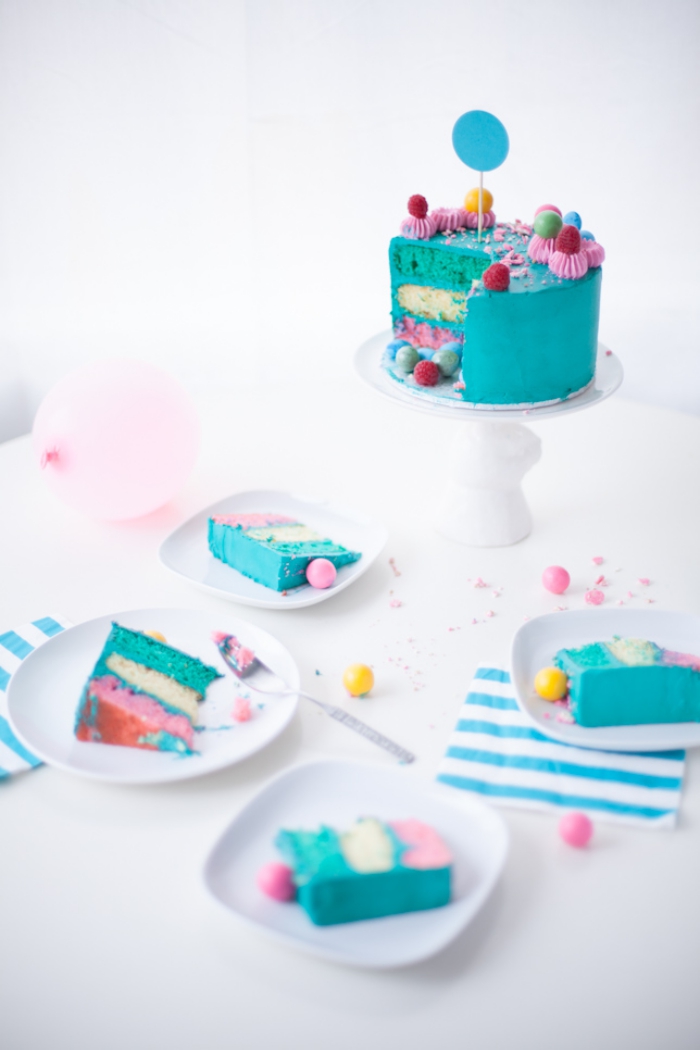 recette de layer cake à plusieurs couches colorées , recouvert de glaçage turquoise et décoré aves des fleurs en glaçage