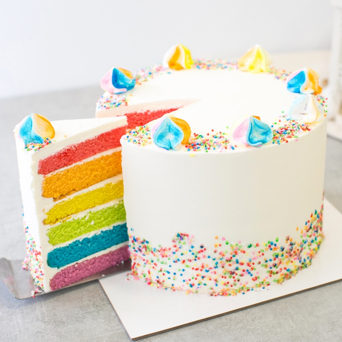 recette de layer cake à base de plusieurs génoises colorées, au glaçage simple à l'extérieur, décoré avec des meringues