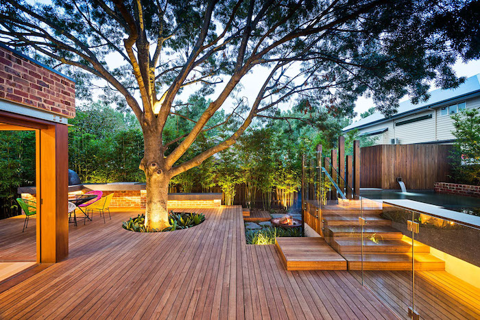 idée terrasse bois composite avec un grand arbre au milieu, cloture bois bordé de bambous, éclairage extérieur moderne