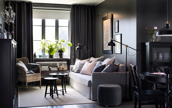 aménagement de salon aux murs foncés avec canapé gris clair couvert de coussins en couleurs pastel et meubles de bois peint noir
