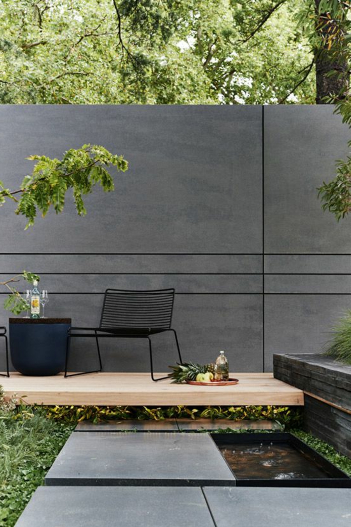 deco mur exterieur en gris anthracite avec des lignes graphiques sur sa largeur, fauteuil en métal noir, table en rotin noire, revetement du sol en bois clair