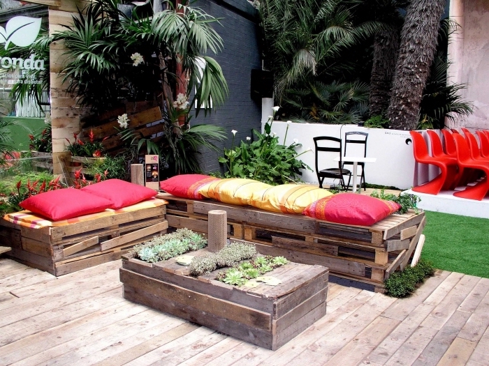 ambiance estivales dans un jardin au plancher de bois aménagé avec meubles en palette à design récup et plantes vertes