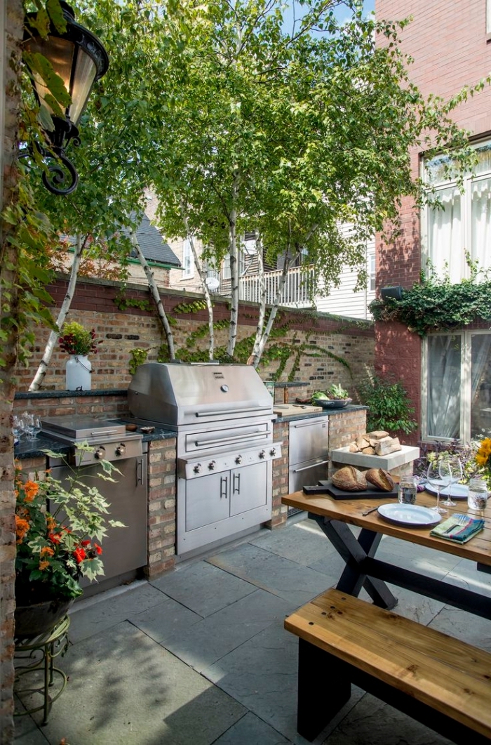 déco de cuisine ouverte dans le jardin avec ilot en pierre et équipement barbecue en acier inoxydable, table à manger bois et noir