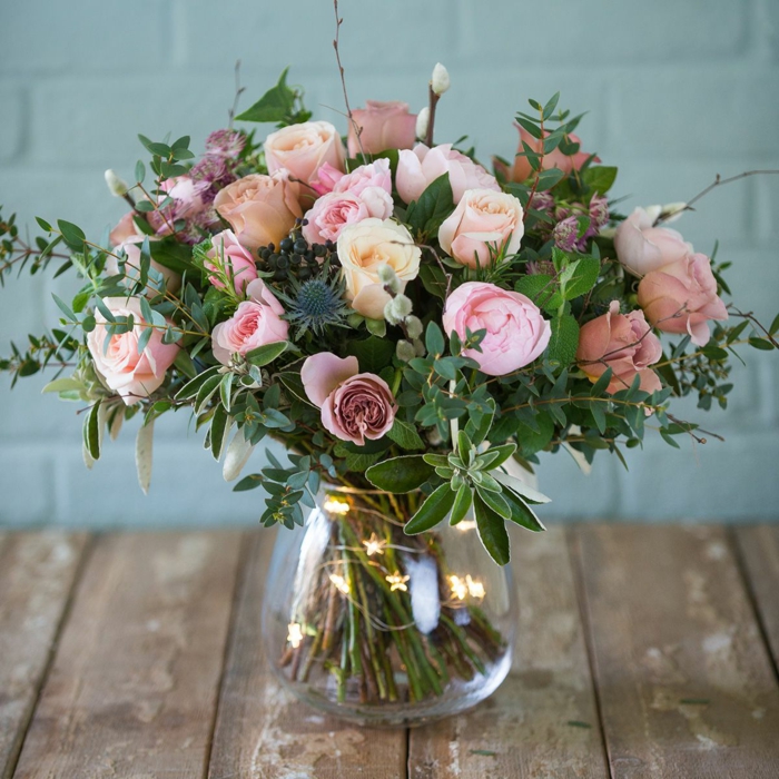 vase en verre, guirlande lumineuse et grand bouquet de roses pastels, plusieurs brins verts