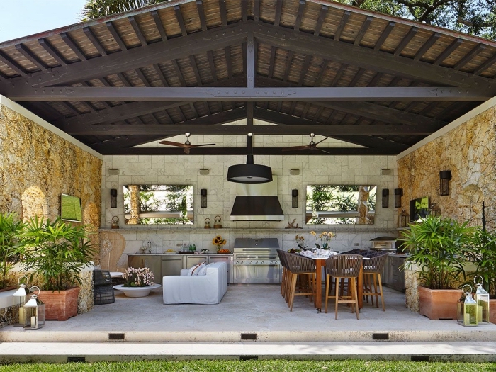modele de cuisine aménagée dans le jardin avec toit de bois massif foncé et murs en pierre, salon de jardin avec canapé blanc