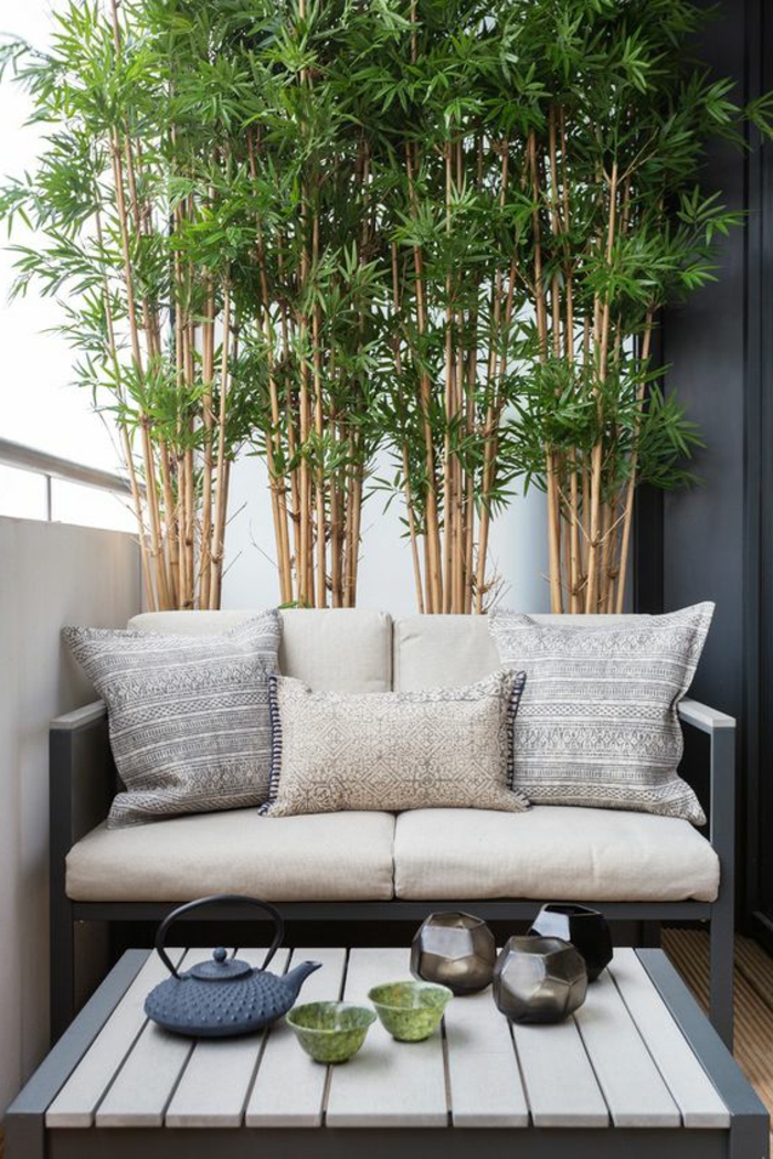 terrasse d'appartement, décoration d'un mur avec des cannes de bambou vertes, aménagement extérieur maison avec canapé trois places et pleins de coussins de taille diverse, petite table basse carrée en bois PVC blanc et bleu canard 