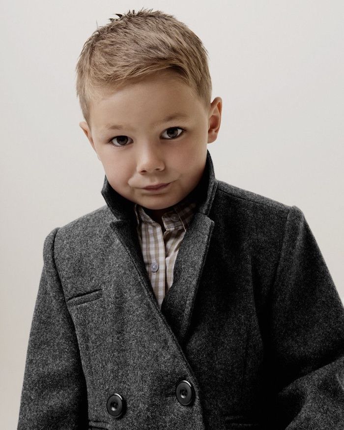 garçon avec une coupe courte, dotée d une frange courte de coté, chemise à carreaux, manteau gris
