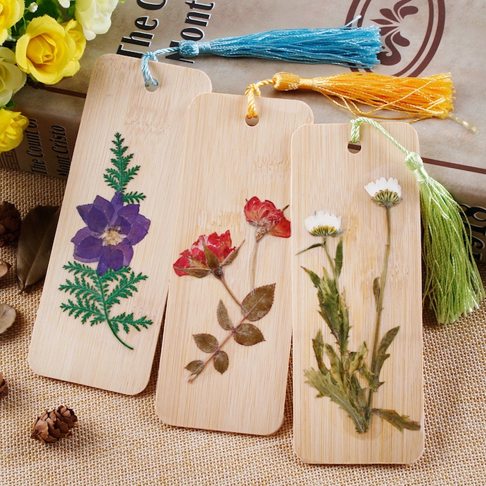 marque page en blocks de bois plats avec décoration de fleurs séchées appliquées avec de la colle et pompon à franges de laine colorée