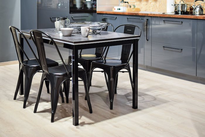 cuisine équipée moderne avec des chaises et table noires et un meuble cuisine gris, doté de plan de travail bois, sol parquet clair