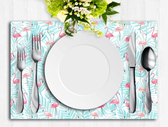 table avec des assiettes et des instruments pour manger, cuillères, fourchettes et couteaux, couvert en bleu turquoise aux flamants roses motifs, déco flamant rose