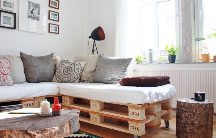 ambiance comfy dans un salon aux murs blancs et au parquet de bois clair aménagé avec canapé d'angle en palettes