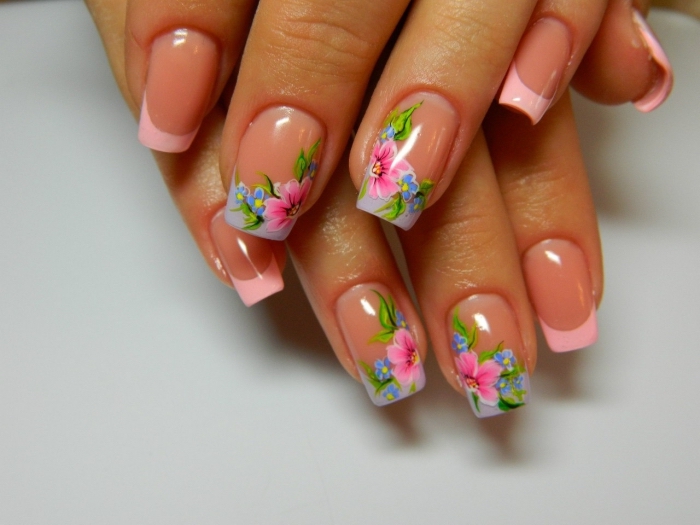 modèle de nail art de style français avec vernis rose pastel sur les bouts des ongles et déco florale en dessin rose vert et bleu