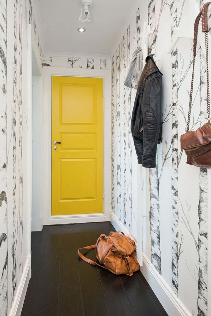 idée originale pour décorer une entrée en jouant sur le contraste de la porte interieur jaune et le revêtement de sol noir, et sur l'originalité du motif du papier peint