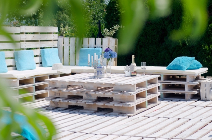ambiance marine dans un coin extérieur aménagé avec bancs couverts de coussins bleus et table en palette sur un plancher de bois