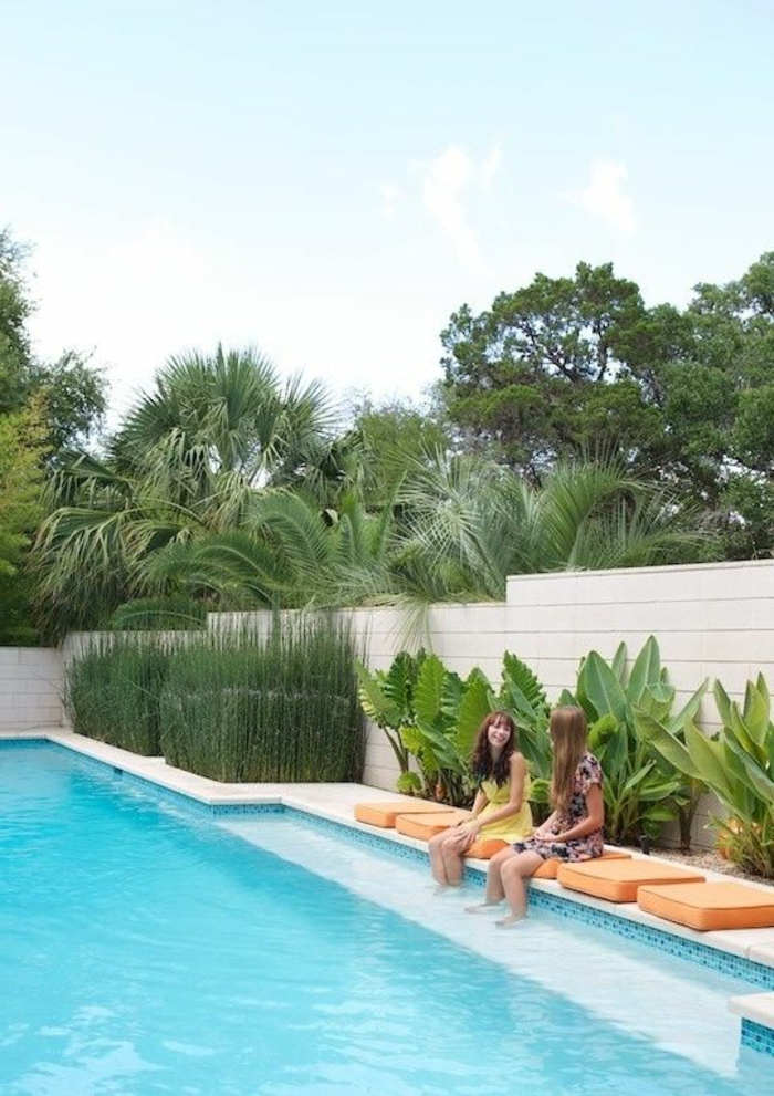 aménagement extérieur maison, idee deco jardin exterieur, habiller un mur extérieur en bois PVC couleur ivoire, grande piscine et coussinets carrés en orange autour de l'eau